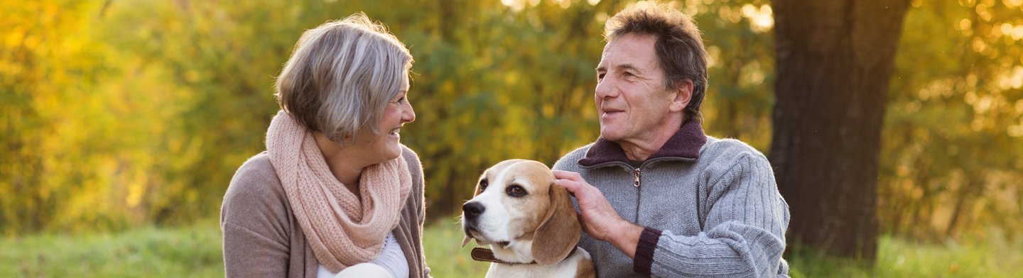 Ein älteres Paar sitzt mit einem Beagle auf einer Wiese