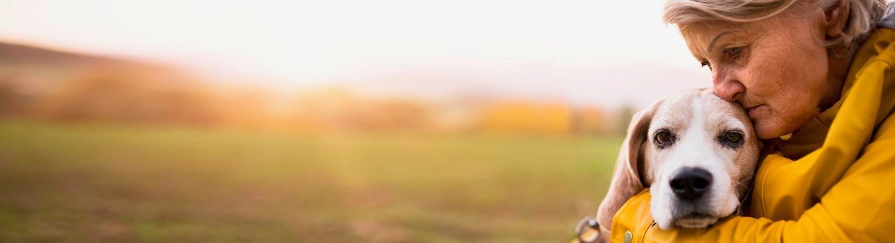 Eine traurig schauende Frau hält ihren Hund im Arm