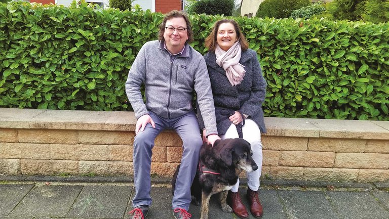 Ein Paar sitzt mit seinem Hund auf der Mauer vor einem Haus.