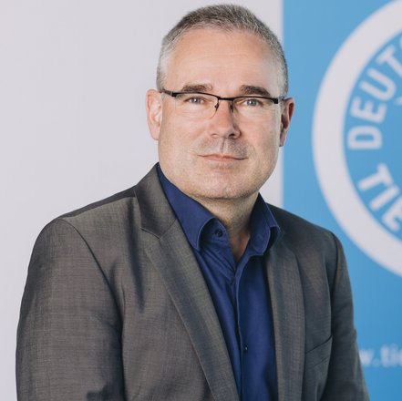 Porträt von Bernd Pieper, der vor dem Logo des Deutschen Tierschutzbundes sitzt