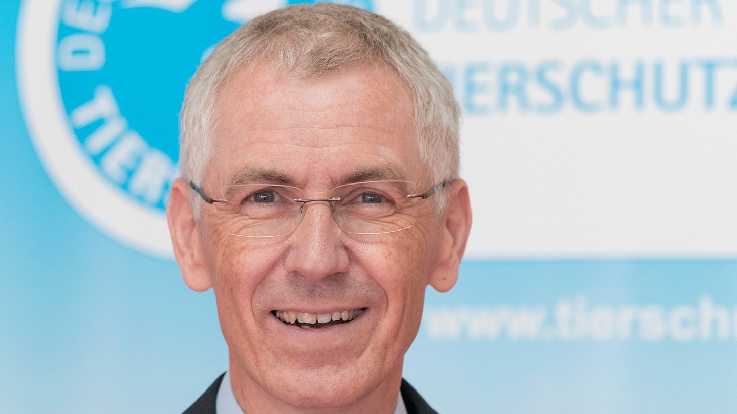Tierschutzbund-Schatzmeister Jürgen Plinz sitzt vor einer Wand mit großem Tierschutzbund-Logo