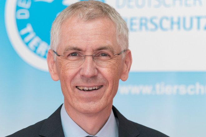 Tierschutzbund-Schatzmeister Jürgen Plinz sitzt vor einer Wand mit großem Tierschutzbund-Logo