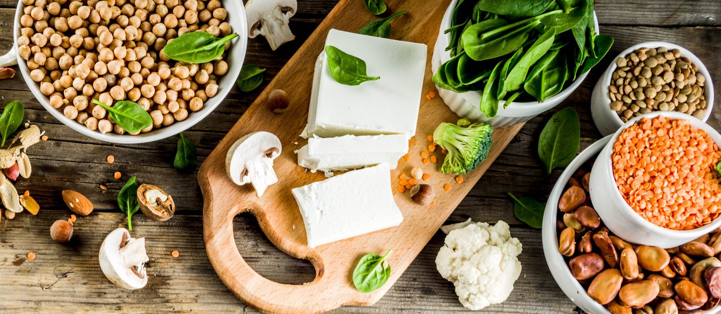 Vegane Proteinquellen auf einem Holztisch: Bohnen, Linsen, Tofu, Sojamilch,Nüsse, Samen und Gemüse